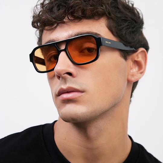 Model wearing black pilot frame with electric-orange lenses